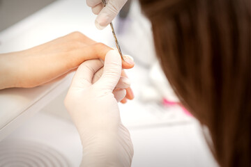 Close up of manicure master with manicure scissors removes cuticles on female nails at a beauty salon
