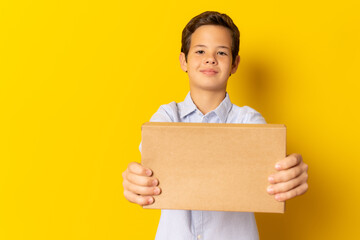 Child boy smiling in blue shirt holding carton box isolated over yellow background.