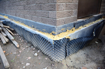 Foundation insulation as a part of house construction. A close-up of an insulated foundation with layers of sprayed tar, polystyrene foam boards, and a bitumen waterproofing membrane.