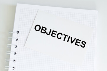 Text OBJECTIVES on a white card on a notebook on a light table