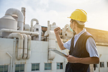 Male worker wearing a yellow helmet with a clipboard works in an industrial factory.