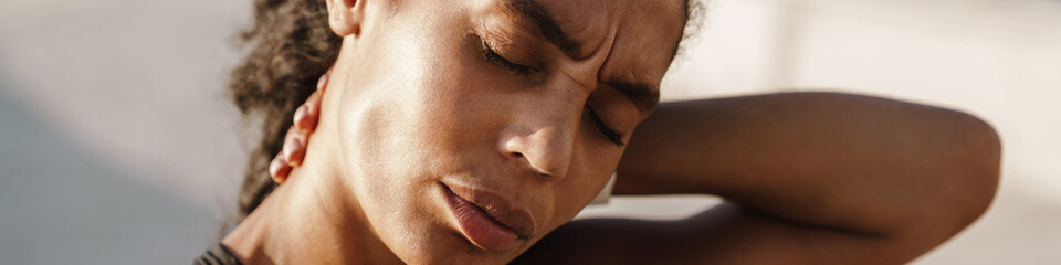 Black sportswoman rubbing her neck while working out on parking