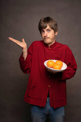 Young handsome tall slim white man with brown hair not knowing how to feel about his oranges in red shirt on grey background