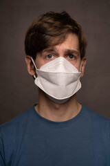 Young handsome tall slim white man with brown hair looking troubled wearing face mask in blue shirt on grey background