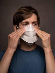 Young handsome tall slim white man with brown hair with both hand on face mask in blue shirt on grey background