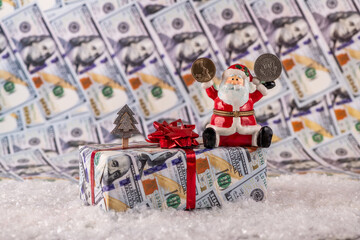 Ceramic figurine of Santa Claus holding in one hand 1 wshddfk coin, and in the other half a dollar against the background of dollar bills and Christmas attributes