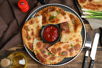 Delicious fried chebureki with ketchup served on wooden table, flat lay