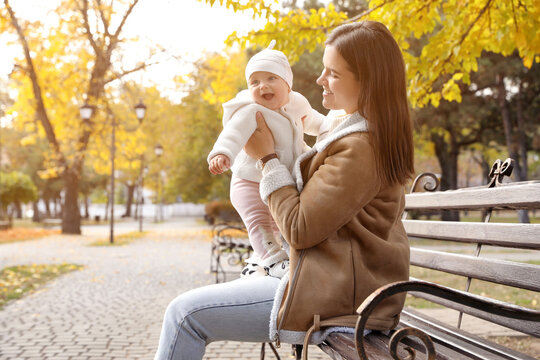 Happy mother with her baby daughter on bench in autumn park, space for text