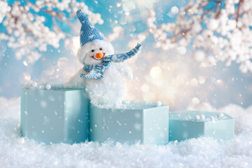 Funny Snowman on blue podiums over winter snowy background with snowy tree branches. Winter concept