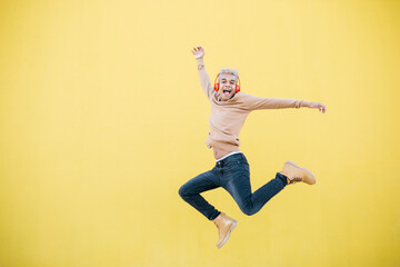 Fototapeta na wymiar Portrait of Smiling Young man using red headphones and jumping Against yellow Background