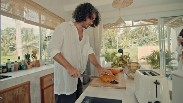 Young happy active married couple dancing laughing together cooking meals at home, carefree joyful husband and wife have fun cooking healthy breakfast food in boho styled kitchen