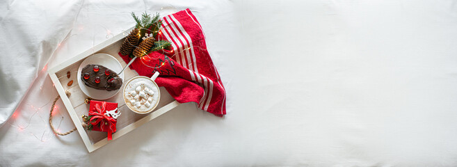 Christmas breakfast in bed with white pastel linen. Banner. Festive breakfast at the hotel. Christmas breakfast on a white wooden tray decorated with festive decor and garland.