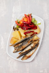 fried sardines with boiled potato and salad on white dish