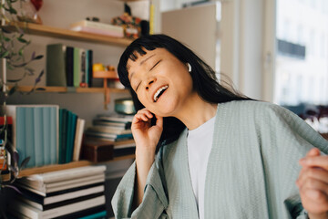 Young woman listening music through wireless in-ear headphones at home