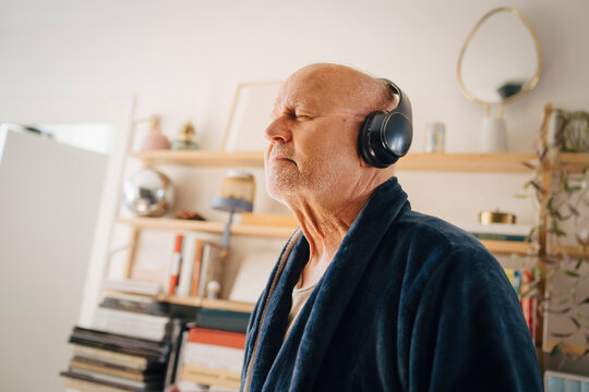 Senior man listening music with eyes closed through headphones at home