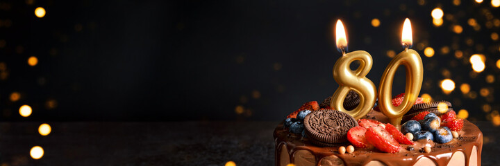 Banner with Chocolate birthday cake with berries, cookies and number eighty golden candles on black...