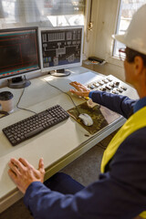 Close up of matured man sitting at the table with control panel and computers while controlling production process at plant