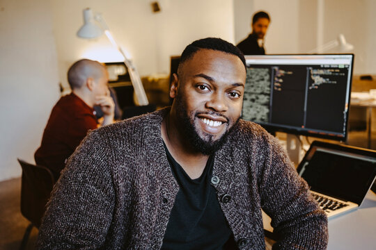 Portrait of young male programmer by colleague working at desk in startup company
