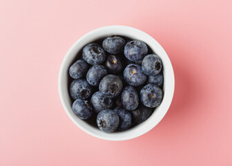 Blueberry in white bowl on pink background.