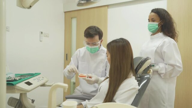 A caucasian dentist man, people showing how to use dental floss with typodont teeth model to Asian patient at hospital clinic. Cleaning. Doctor. Dentistry, medical and health.