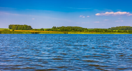 Summer landscape with a river on a background of blue sky with white clouds