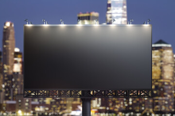 Blank black billboard on city buildings background at night, front view. Mockup, advertising concept
