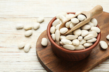 Bowl and scoop with uncooked white beans on wooden table, space for text