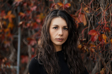 Close up Portrait of a young brunette woman against the background of a burgundy autumn landscape
