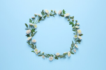 Wreath made of beautiful flowers and green leaves on light blue background, flat lay. Space for text