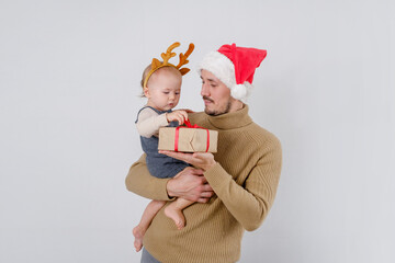Obraz premium A funny baby being hold by father wearing Santa Claus hat unpacks a Christmas box
