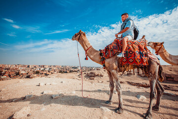 European male tourist sits on a camel and rides near the pyramid of Giza - Cairo, Egypt