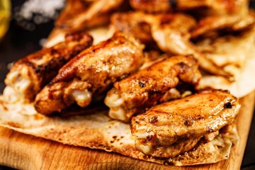 BBQ chicken thighs. Appetizing grilled poultry meat on a wooden cutting board. Dark rustic background. Close-up. Soft focus. Food photography