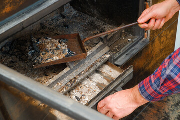 Ash removal from the fireplace. A man's hand in a plaid shirt holds a shovel with ash from the fireplace. A man cleans the fireplace.