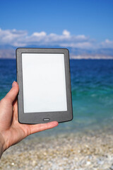 hand holding e-book reader on the beach, reading during summer vacation