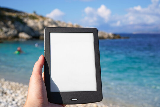 hand holding e-book reader on the beach, reading during summer vacation