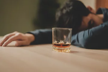 Foto op Canvas Alcoholism, depressed asian young man sleep on table while drinking alcoholic beverage, holding glass of whiskey alone at night. Treatment of alcohol addiction, suffer abuse problem alcoholism concept © KMPZZZ