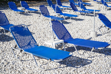 empty sunbeds on  white pebbles on Bataria Beach in Kassiopi, Corfu island, Greece