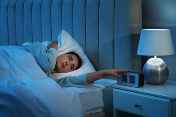 Unhappy young woman covering ears with pillow in bed at home. Noisy neighbours