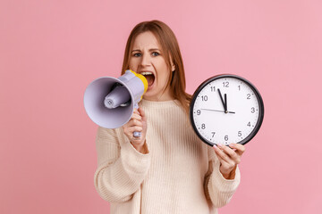 Portrait of serious young adult blond woman screaming in megaphone, looking at camera and holding...