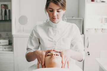 Beautician rubbing client forehead, making relaxing head massage in spa salon. Skin care concept