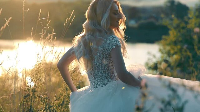 Pretty bride running to the lake on a background of sunset. Moranrange sunset and rays on the backlight. young woman in long chiffon dress