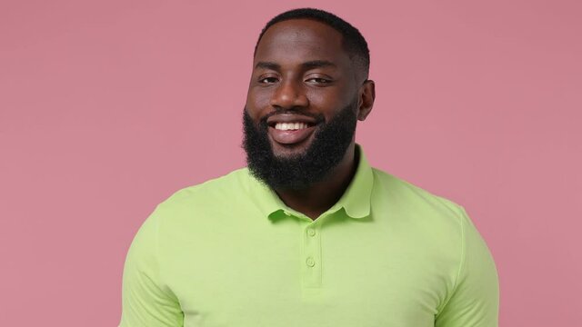Puzzled confused astonished joyful satisfied young bearded african american man 20s wears green t-shirt look around think dream nodding isolated on plain pastel light pink background studio portrait