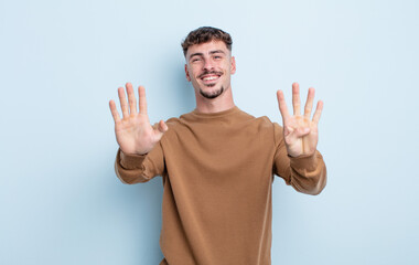 young handsome man smiling and looking friendly, showing number nine or ninth with hand forward,...