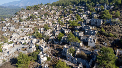 Obraz premium Historical Lycian village of Kayakoy, Fethiye, Mugla, Turkey. Drone aerial shot from above of the Ghost Town Kayakoy. Greek Village. Evening moody warm sun of the ancient city of stone