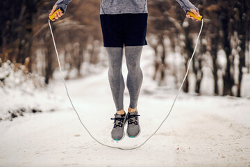 Legs jumping the rope on snowy path at winter. Winter sport, cardio exercises, healthy habits