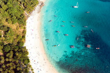 View from above, stunning aerial view of a white sand beach bathed by a turquoise, clear water. Tropical beach with some long tail boats and relaxed tourists. Freedom beach, Phuket, Thailand. - obrazy, fototapety, plakaty