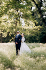 the groom and the bride are walking in the forest near a narrow river