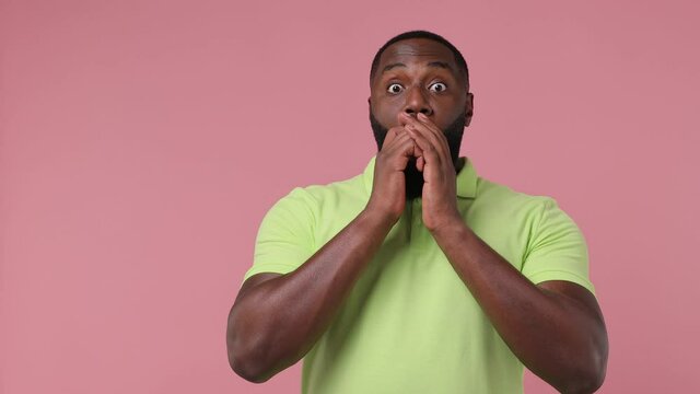 Promoter amazed young american man 20s wears green t-shirt point finger look aside on workspace copy space mockup promo commercial area isolated on plain pastel light pink background studio portrait