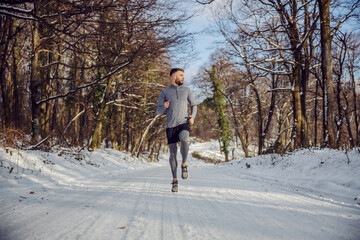 Fit runner running in forest at sunny snowy winter day. Outdoor fitness, cardio exercises, winter fitness