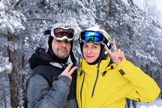 Happy middle-aged Caucasian man and woman in ski helmets and goggles on the background of a snowy forest. Active winter rest. Bright clothing for an active lifestyle and winter sports. Winter season.